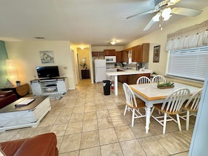 A compact living space with a TV, seating area, dining table, kitchen, and a ceiling fan.