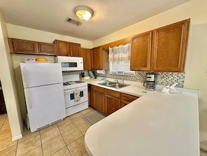 A kitchen with wooden cabinets, a white refrigerator, a microwave, a stove, and a coffee maker.