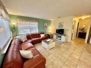 A living room with a brown leather sofa, a white coffee table, and a television on a wooden stand.
