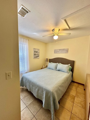 A bedroom with a bed, a ceiling fan, a window with blinds, a wall-mounted light, and a sign that says "Florida".