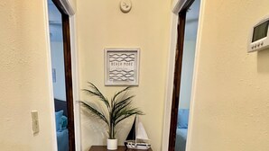 A hallway with a door leading to a room, a small cabinet with a plant, a framed picture on the wall, and a thermostat. - #8 2-bedroom cottage in Salt Springs Under New Management, ice machine on site. (Salt Springs)