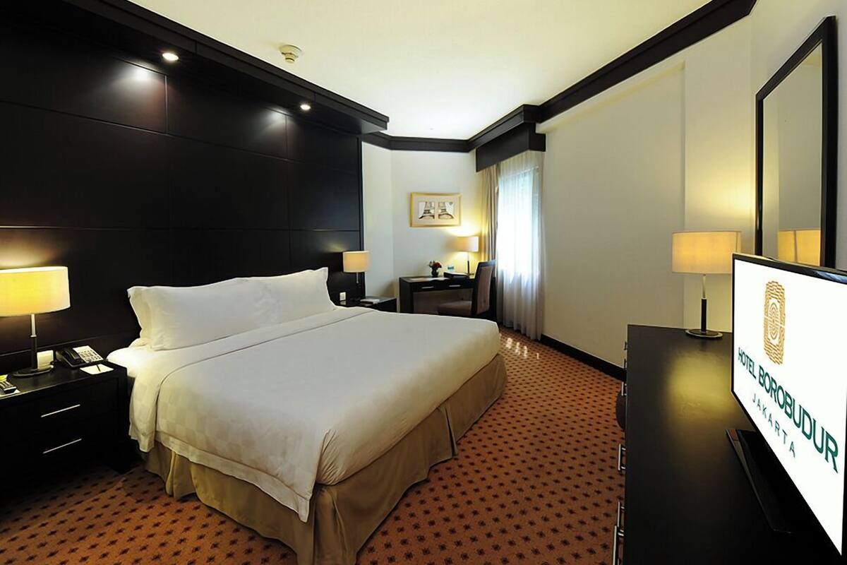 Habitación de hotel con una cama grande, lámparas de noche, un escritorio con silla, un televisor de pantalla plana y un cuadro en la pared.