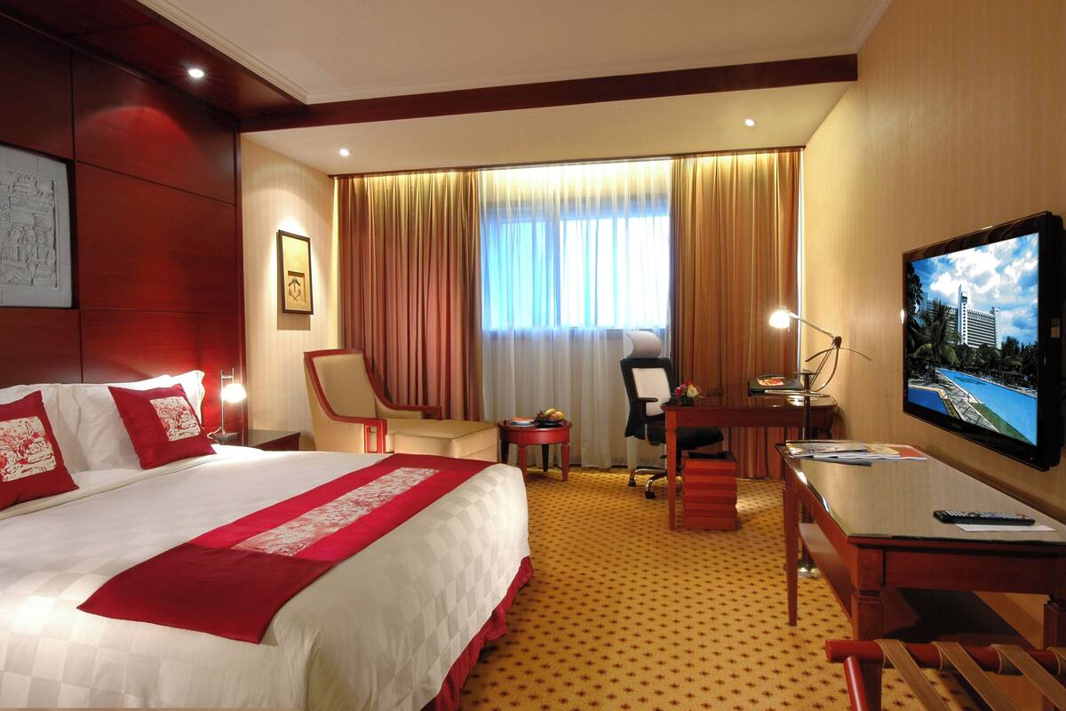 Habitación de hotel con una cama grande, un escritorio con computadora, televisor y una silla.