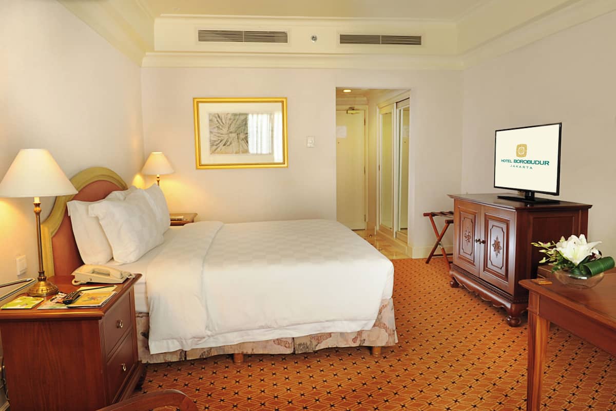 Habitación de hotel con cama, lámparas de noche, teléfono, televisor y un cuadro en la pared.