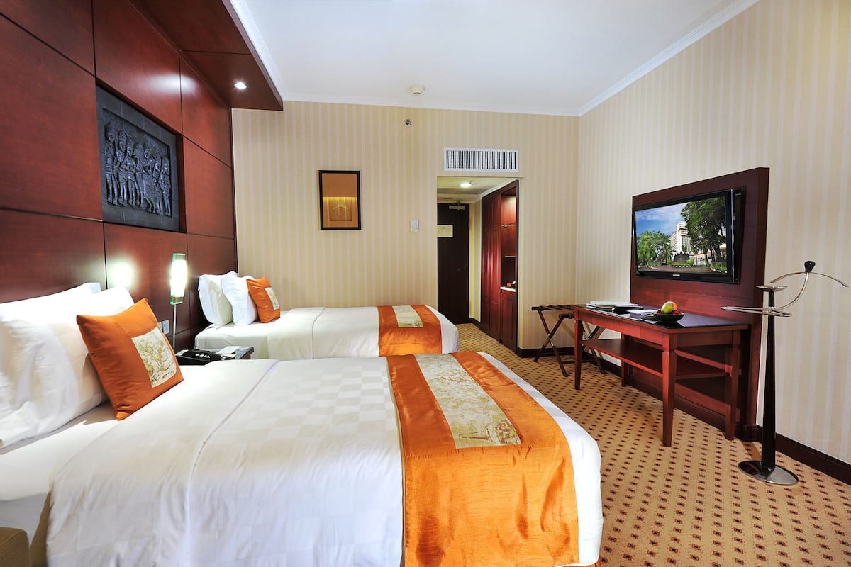 Una habitación de hotel con dos camas, un escritorio, un televisor y una puerta que da a otra habitación.