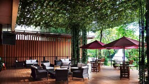An outdoor patio area with wooden flooring, wicker furniture, and red umbrellas providing shade. - Hotel Borobudur Jakarta (Jakarta)