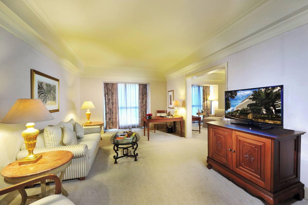 Habitación de hotel con sala de estar que incluye un sofá, una mesa de centro, un televisor sobre un mueble y una mesa de comedor con sillas.