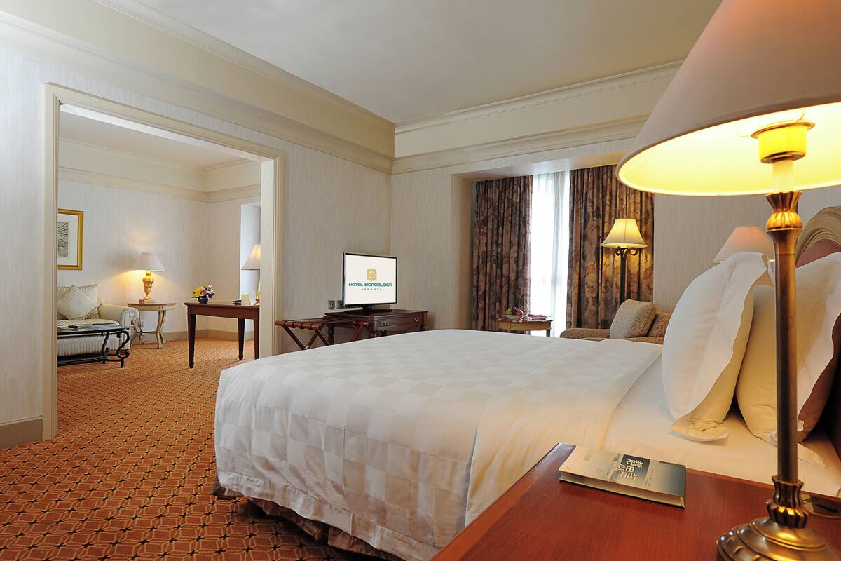 Habitación de hotel con una cama grande, un escritorio con una computadora, una silla, una lámpara y vistas al exterior a través de una ventana.