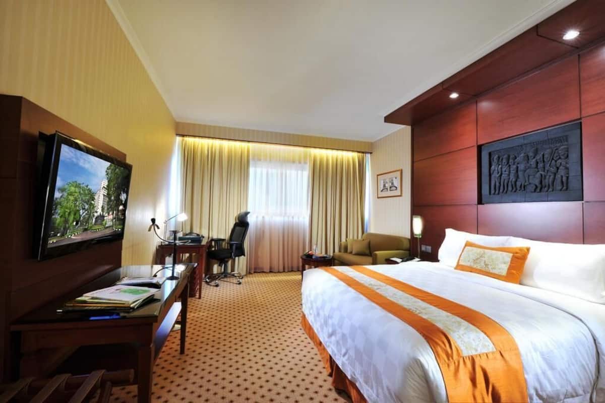 Una habitación de hotel con cama, escritorio, silla, televisor y cortinas.