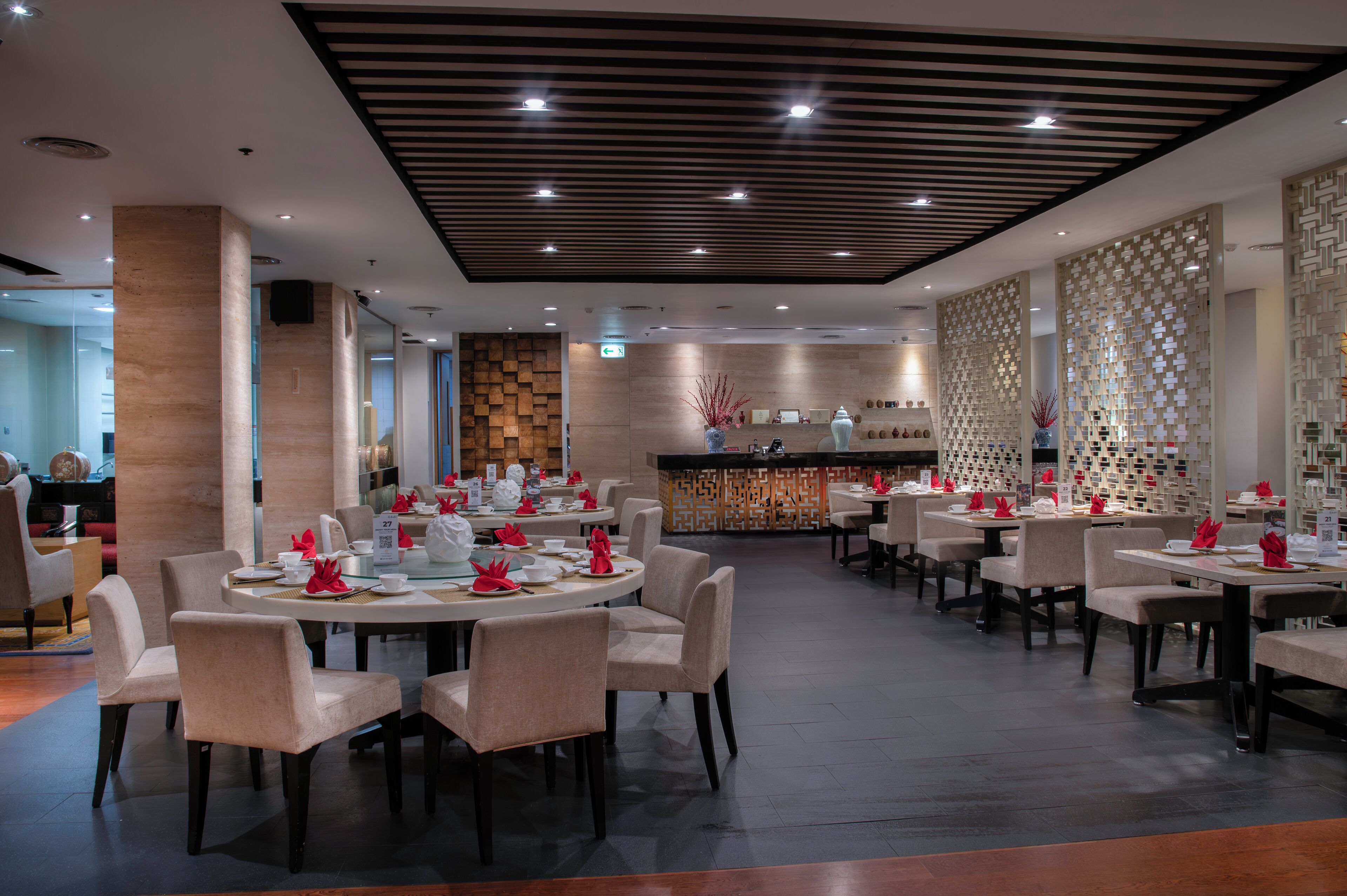A modern restaurant with round tables and chairs, a wooden accent wall, and a decorative partition with hanging elements.