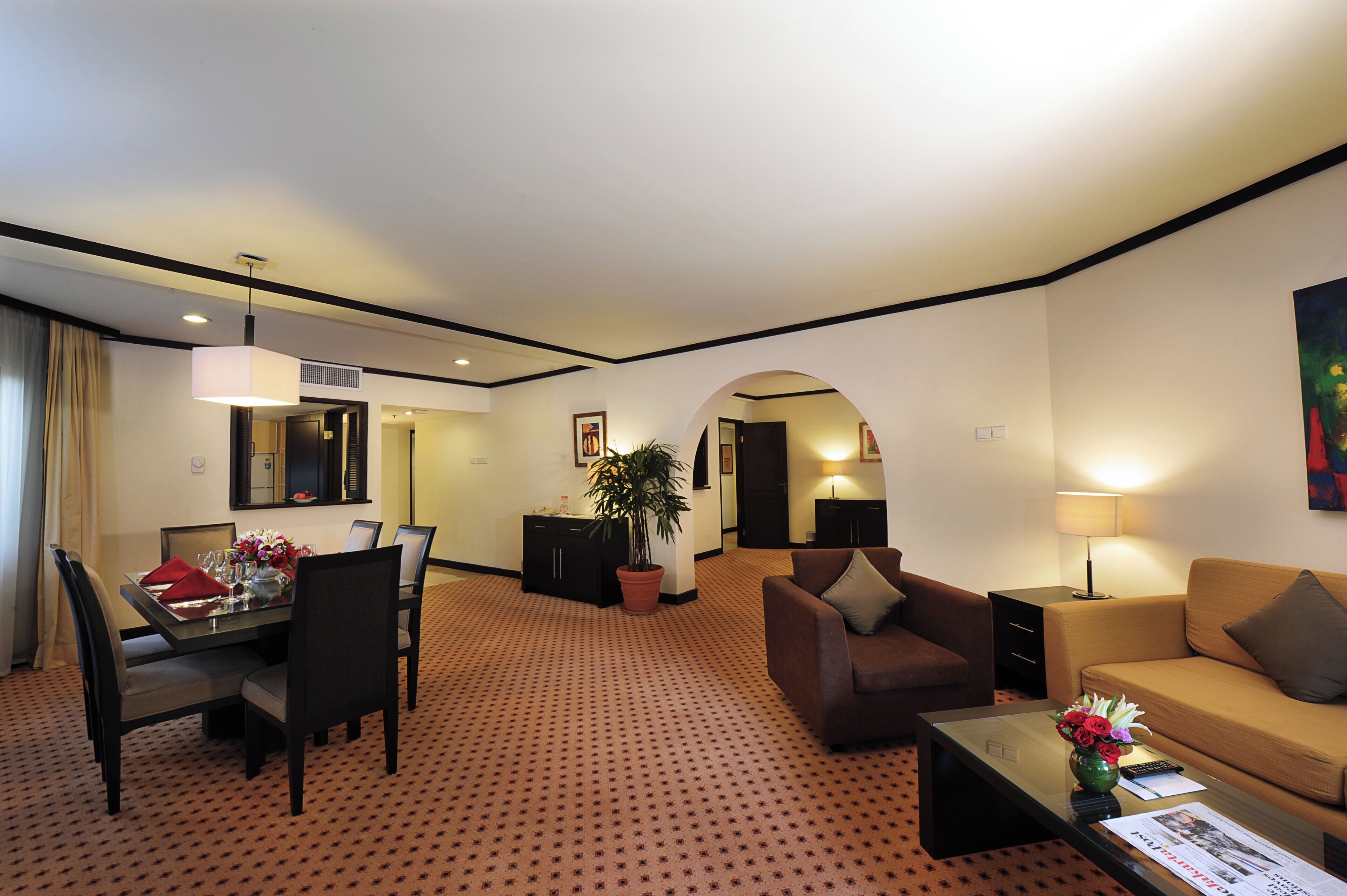 A hotel room with a dining area, a sofa, a coffee table, and a potted plant.