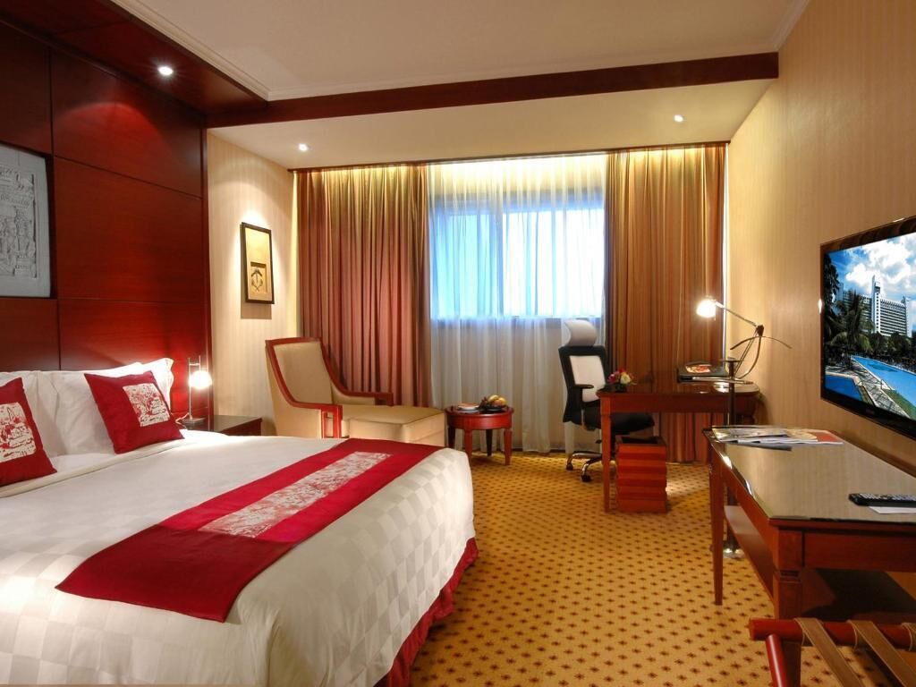 Habitación de hotel con una cama grande, un escritorio, una silla, un televisor y una ventana con cortinas.