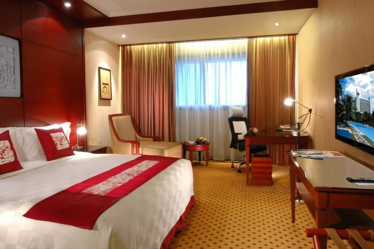 Habitación de hotel con una cama grande, un escritorio, una silla, un televisor y una ventana con cortinas.