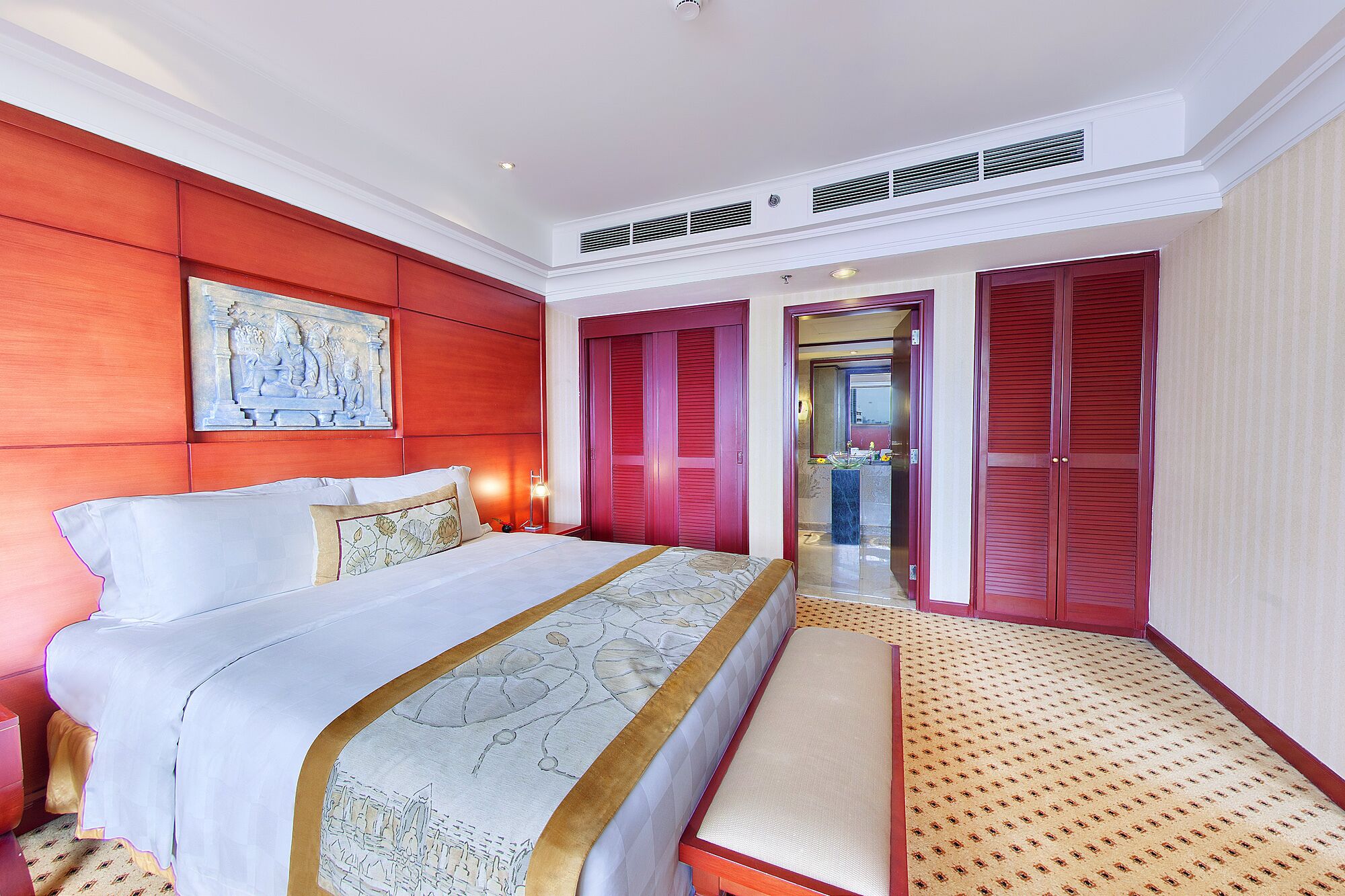 Hotelkamer met een groot bed, een bankje, een schilderij en uitzicht op de badkamer.