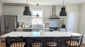 A modern kitchen with a large island, stainless steel appliances, and pendant lighting. - Modern Raleigh Downtown Rooftop Skyline View SFH-R (Raleigh)