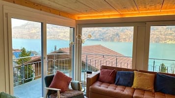 Uma sala de estar acolhedora com sofá de couro, uma poltrona, mesa de centro e vista para um lago através de grandes janelas.