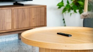 En moderne stue med et fladskærms-tv på et træskab, et rundt træsofabord og en potteplante.