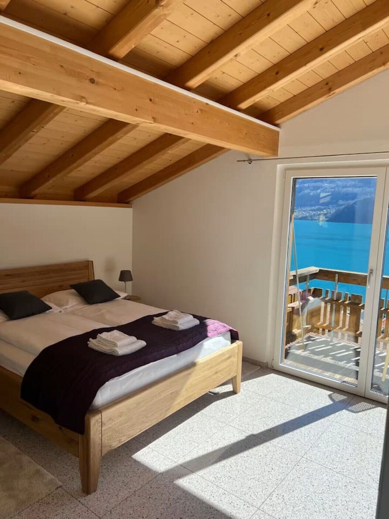 Ein Schlafzimmer mit Holzboden, einem Bett mit Kissen, einer Decke und Meerblick durch eine Glastür.