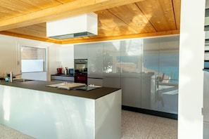 A modern kitchen with a central island, stainless steel appliances, and a wooden ceiling.