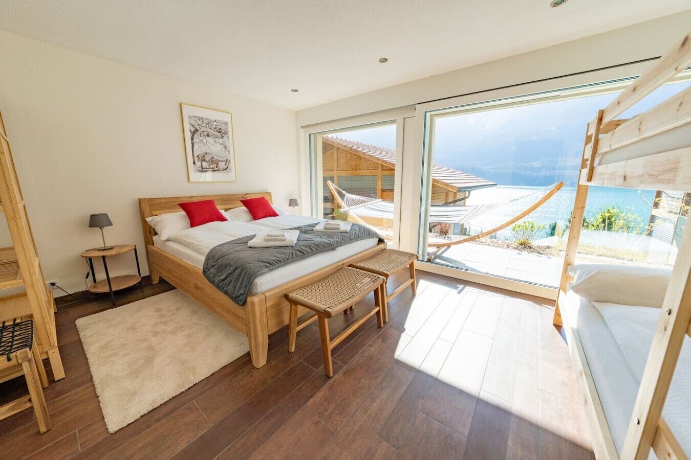 A bedroom with a large bed, a bedside table, a bench, and a view of the outdoors.