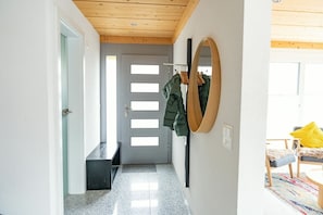 A hallway with a door, a mirror, and a bench.