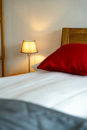 A bed with a white sheet and a red pillow, a wooden headboard, and a floor lamp with a beige lampshade. - Luxury Lakeview SPA Chalet near Interlaken • AC • BBQ by SwissDreamLiving (Niederried bei Interlaken)