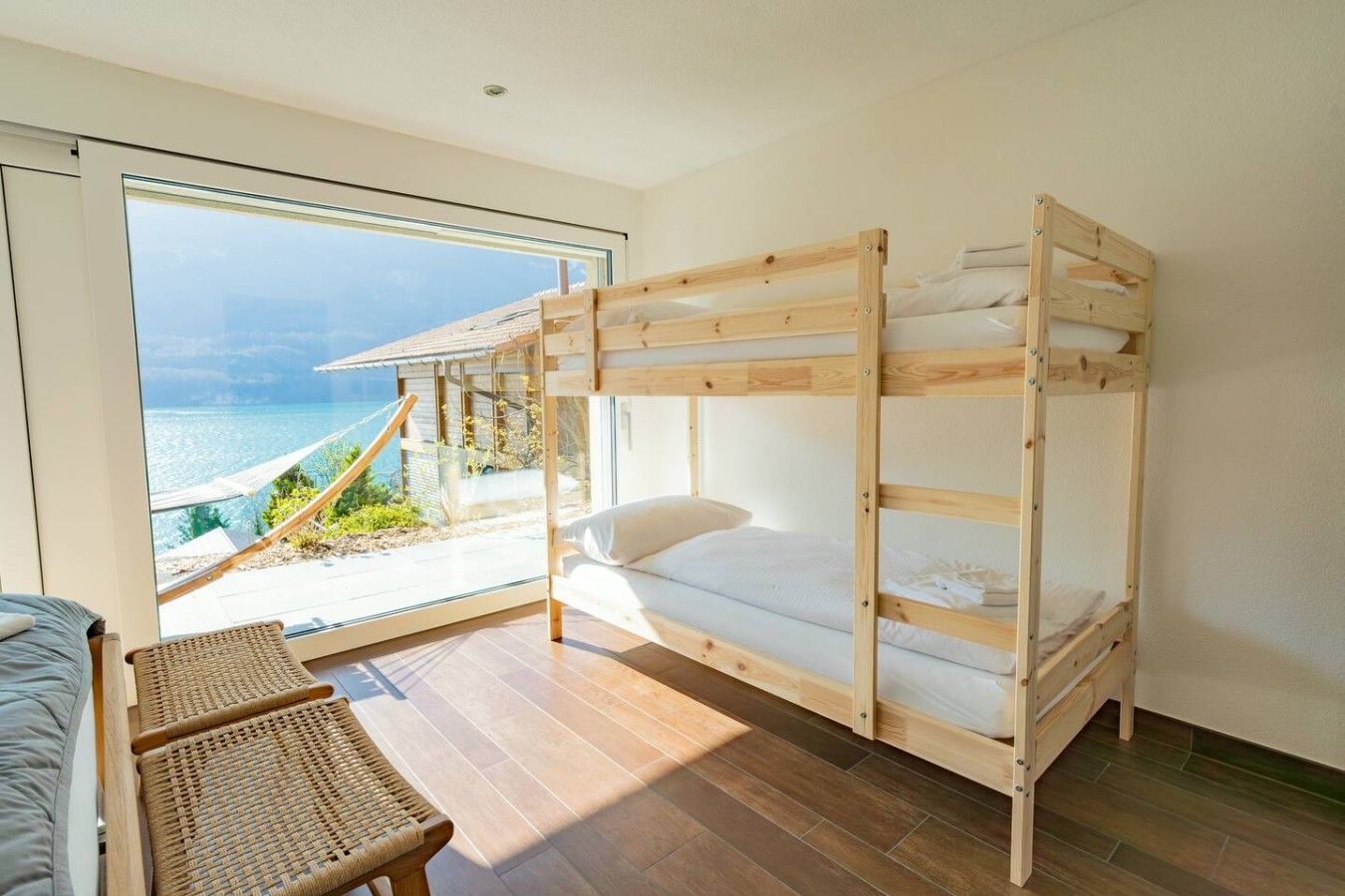 Een slaapkamer met stapelbed en uitzicht op zee, een rieten stoel en een klein tafeltje.