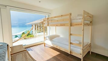 Een slaapkamer met stapelbed en uitzicht op zee, een rieten stoel en een klein tafeltje.