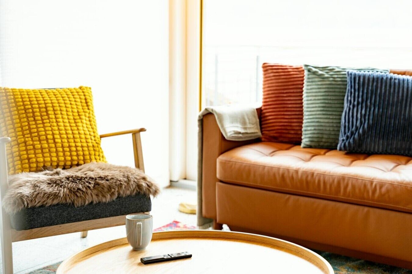 A living room with a sofa, armchair, and a round coffee table with a remote control.