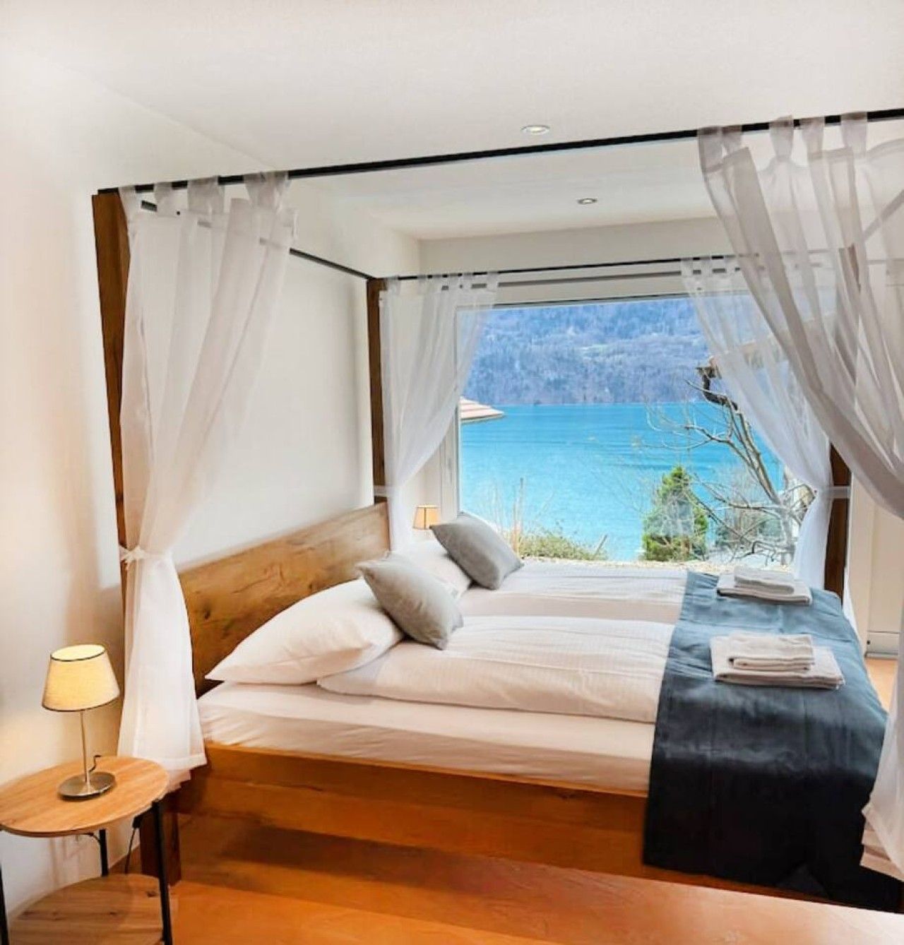 Une chambre à coucher avec un lit, des rideaux, une table de chevet et une vue sur une étendue d’eau.