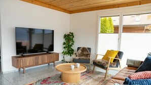 En moderne stue med et fladskærms-tv, et træ sofabord, en sofa og to lænestole.