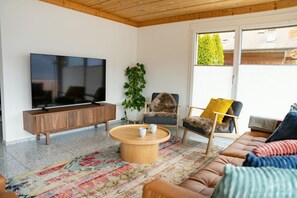 Una sala de estar moderna con un televisor de pantalla plana, una mesa de centro de madera, un sofá y dos sillones.