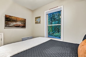 Ein Zimmer mit einem Bett, einem Fenster mit Blick auf Grünflächen, einem Landschaftsbild und einem Schild über dem Fenster.