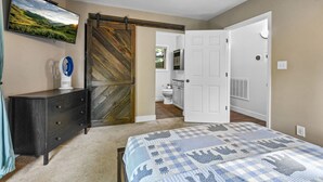 Una camera da letto con un letto, una cassettiera, una televisione e una porta scorrevole in stile rustico che conduce al bagno.