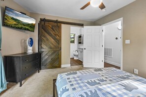 A bedroom with a bed, a dresser, a TV, and a sliding barn-style door leading to a bathroom. - Hot Tub, Mtn Views & EV Charger, 1.5mi to Gatlinburg Strip (Gatlinburg)