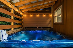 Ein Whirlpool mit Holzterrasse und Lichterketten, umgeben von Holzwänden und einem Fenster.