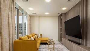 Un soggiorno moderno con un divano giallo, una TV a schermo piatto montata a parete e ampie finestre con tende.