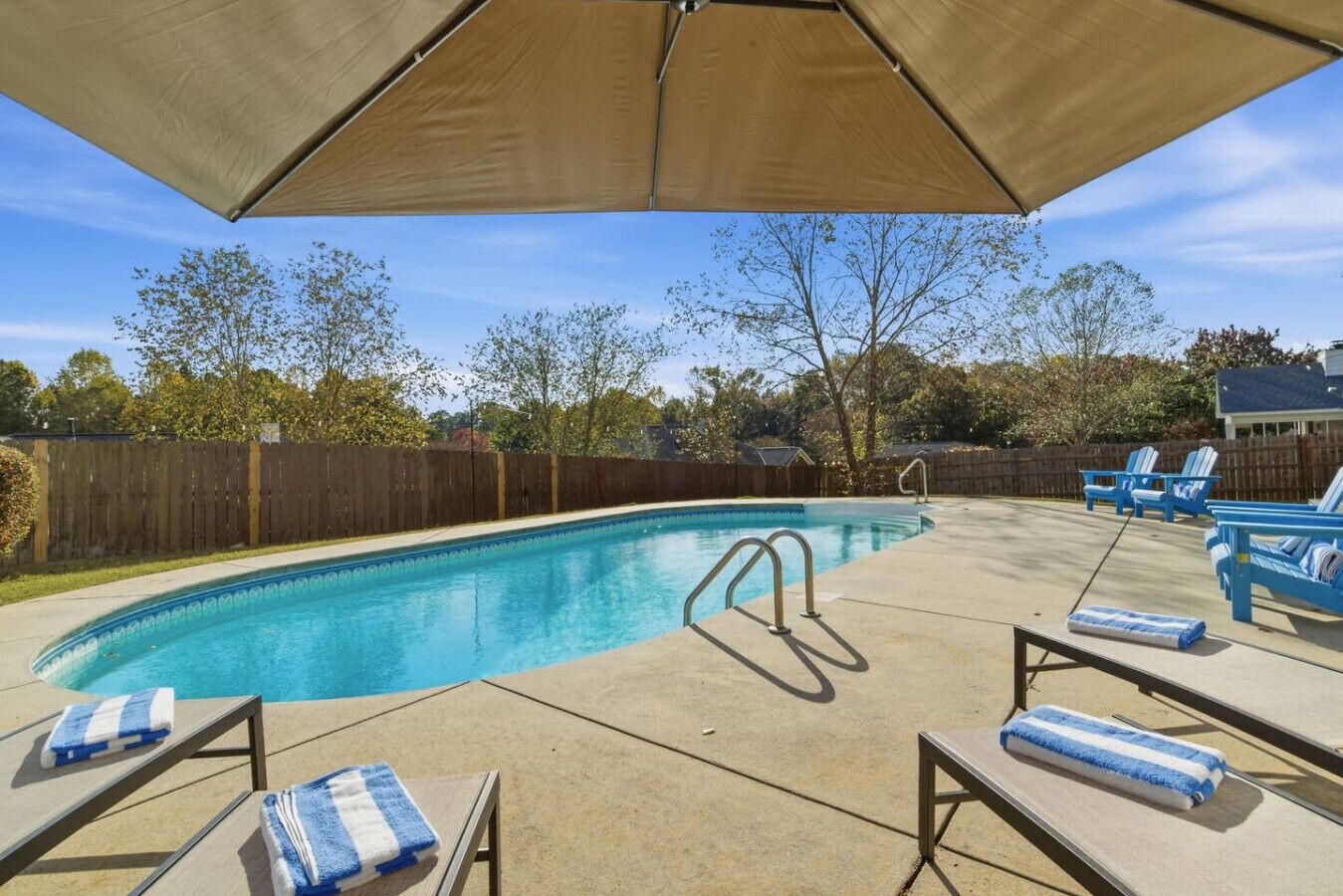 A backyard with a swimming pool, lounge chairs, and a covered patio area.