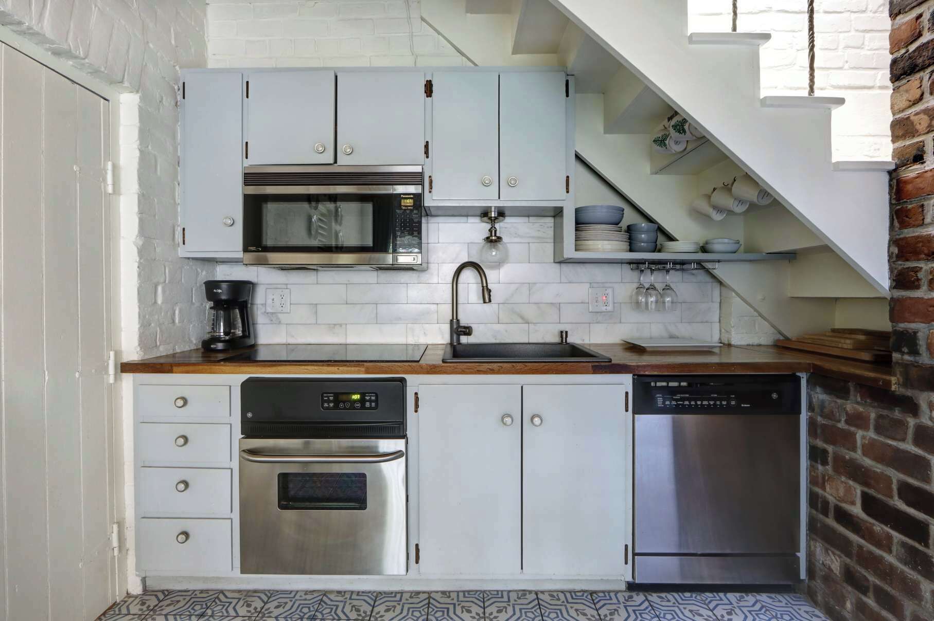 A compact kitchen with white cabinets, a built-in microwave, a stainless steel oven, a dishwasher, and a sink.