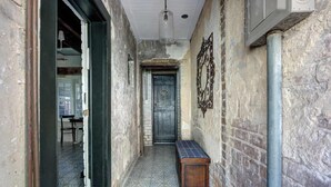 A narrow hallway with patterned floor tiles, a wooden bench, and a metal door with a sign. - The Gaston Loft, Historic | Steps to Forsyth Park (Savannah)