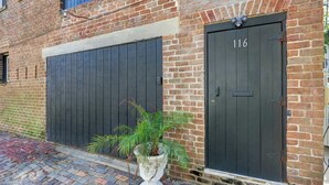 A brick building with two dark-colored garage doors, one with the number 116. - The Gaston Loft, Historic | Steps to Forsyth Park (Savannah)