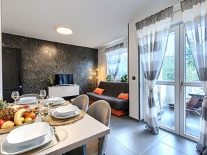 A modern living room with a sofa, dining table set for two, a TV, and a balcony with curtains. - Gordana by Interhome (Labin)