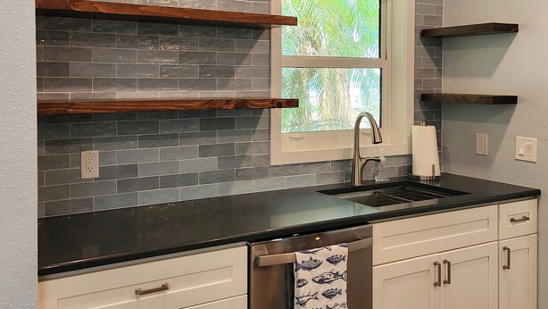 A kitchen with gray tiled backsplash, wooden shelves, a window, and a stainless steel sink. - Cozy 2-bedroom Lakehouse in charming Avon Park (Avon Park)