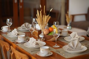 Une table à manger dressée avec de l’argenterie blanche, des serviettes et des verres à vin, agrémentée d’un centre de table composé d’épis de blé séchés et de fruits.
