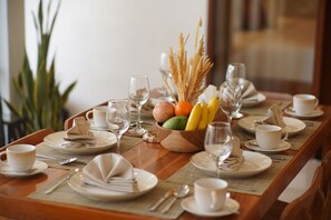 Une table à manger dressée avec des assiettes, des couverts, des verres et un saladier rempli de fruits.