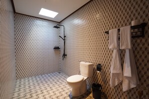 Une salle de bain avec un carrelage décoratif au sol, des toilettes, une douche et un porte-serviettes avec des serviettes.
