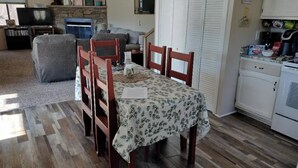 Un comedor con una mesa preparada para cuatro personas, un sofá, un televisor y una zona de cocina con armarios y electrodomésticos.