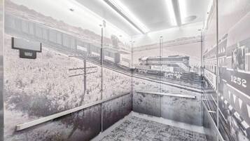 A room with a mural of a train station, a bed, and a nightstand.
