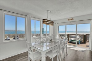 A dining area with a glass table and white chairs, large windows with a view of the beach, and a hanging light fixture. - Point of View- Beachfront, dog-friendly 4-BR townhome with unbeatable views (North Topsail Beach)
