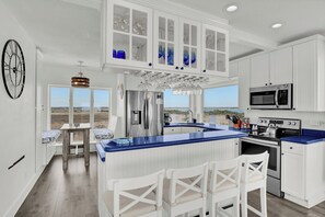 A kitchen with white cabinets, a blue countertop, a stainless steel refrigerator, a microwave, and a stove. - Point of View- Beachfront, dog-friendly 4-BR townhome with unbeatable views (North Topsail Beach)